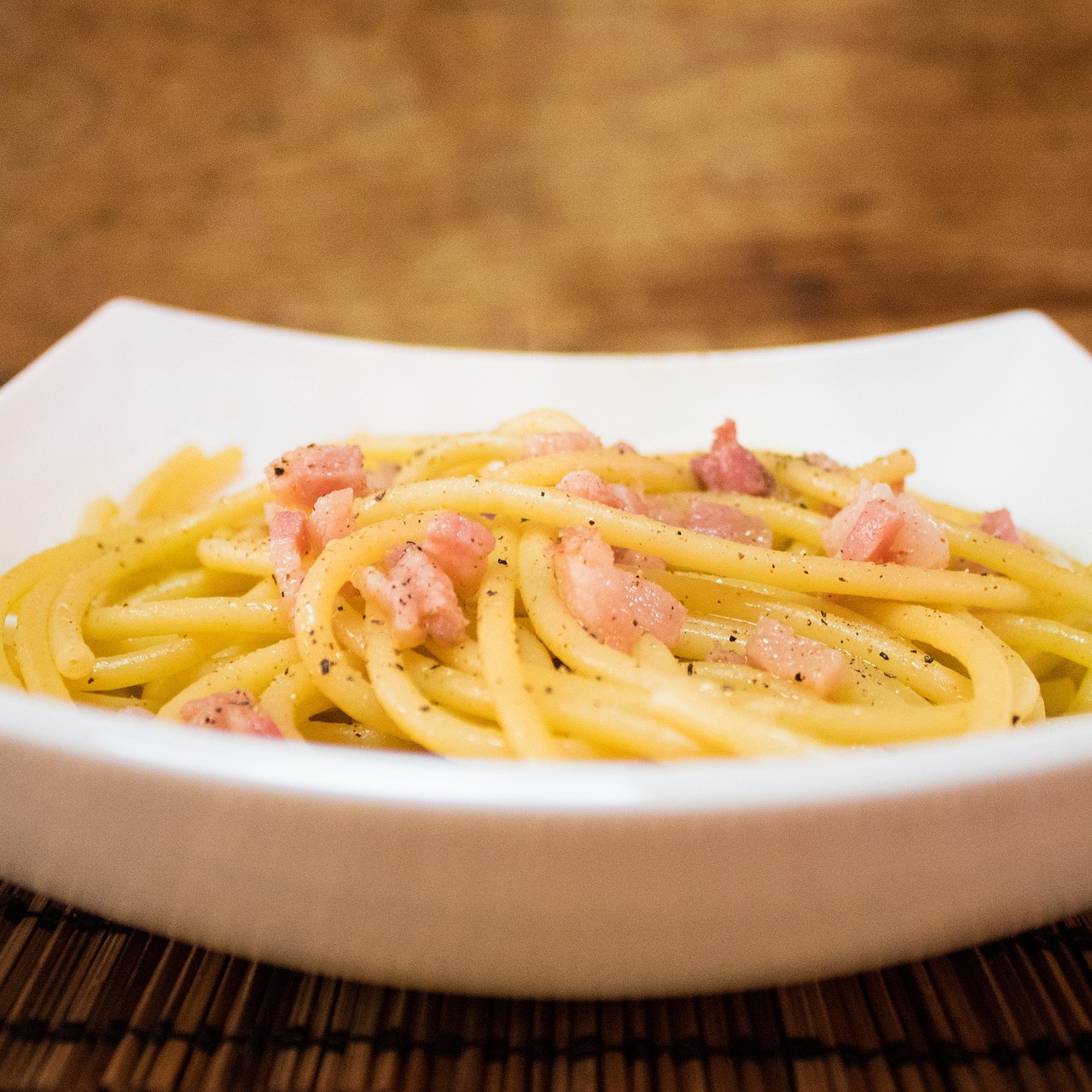 Piatto di pasta alla carbonara con guanciale, uova e pecorino, servito su tavola rustica.