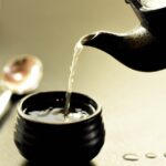 Tazza di tè verde fumante su un tavolo, con un libro e un termometro accanto.